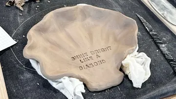 Clay shell dish with engraved text on table.