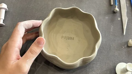 Hand holding clay bowl on worktable.