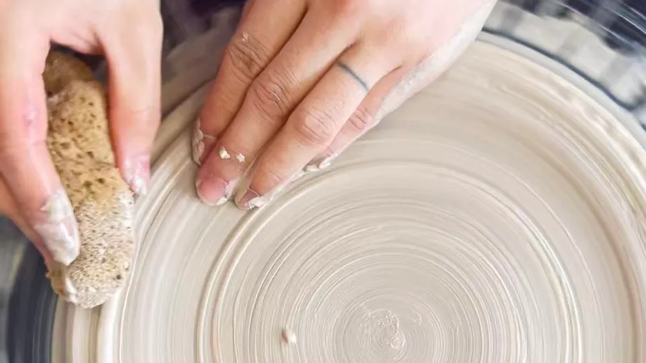 Hands shaping clay with sponge on wheel.