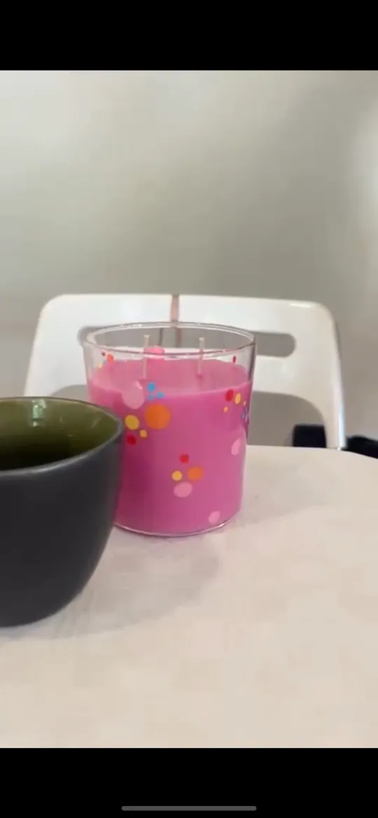 Pinkfarbene Kerze und schwarze Tasse auf Tisch.