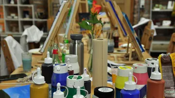 Paint bottles on a busy art table.
