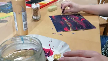 Person malt mit Acrylfarben auf Tisch.