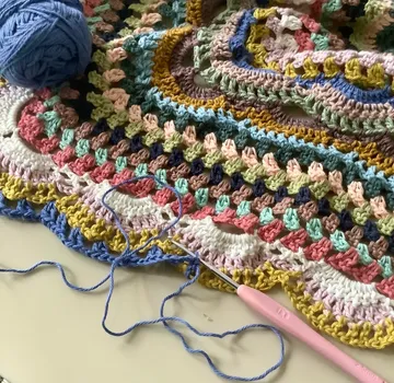 Crocheted blanket with yarn and hook on table.
