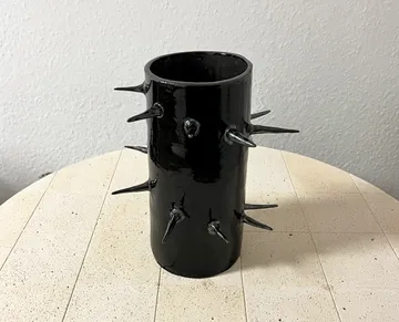Schwarze Vase mit Stacheln auf hellem Tisch.