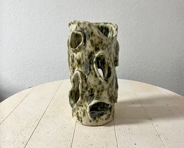 Ceramic vase with holes on wooden table.