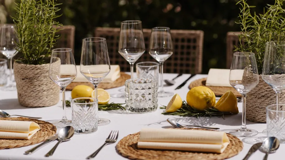 Table with glassware, lemons, and herbs outdoors.