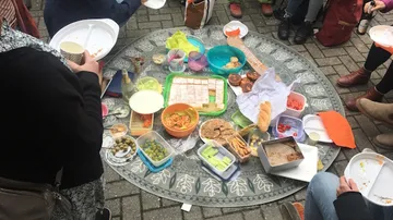 People sharing picnic food on circular cloth.