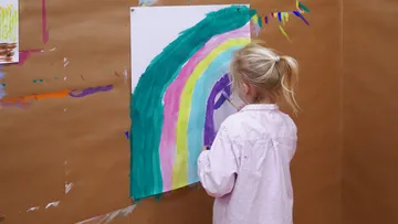 Child painting large rainbow on paper.