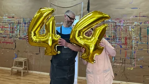 Two people holding gold number balloons indoors.