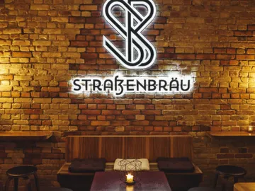 Neon sign shows 'Straßenbräu` on a brick wall.