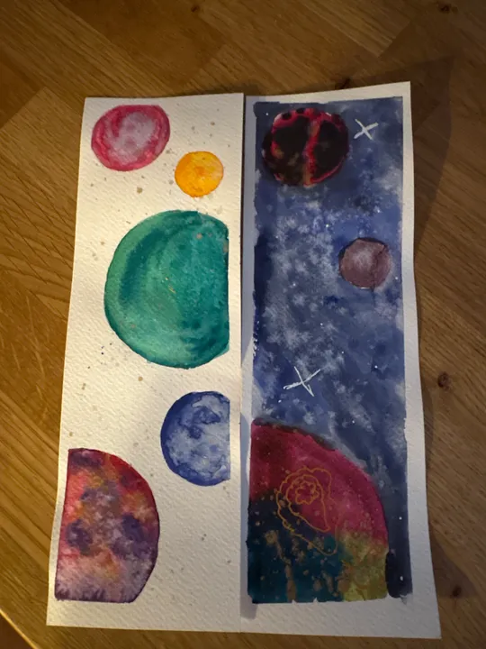 Watercolor planets on paper, wooden background.