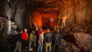 Visitors observe sculptures inside illuminated cave.