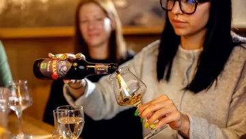 Woman pours beer into glass at bar.