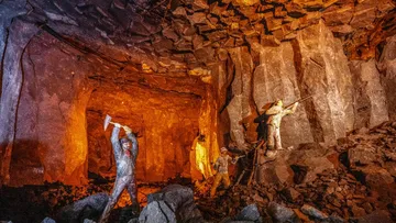 Bergleute mit Werkzeugen in einer schwach beleuchteten Höhle.