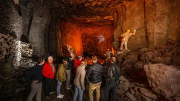 Tourists explore rock cavern with statues around.