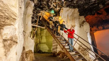 Menschen steigen Treppe in Felsenhöhle hinauf.