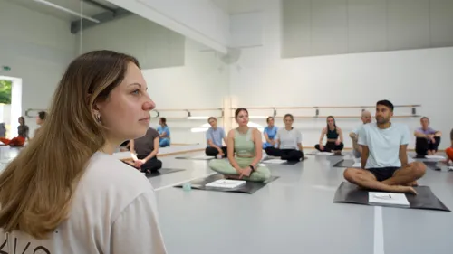 Menschen sitzen auf Yogamatten im Studio.