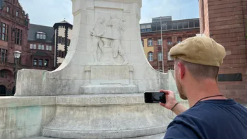 Mann fotografiert Denkmal auf Stadtplatz.