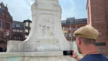 Mann fotografiert ein Denkmal auf Stadtplatz.