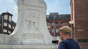 Person fotografiert Statue in städtischer Umgebung.