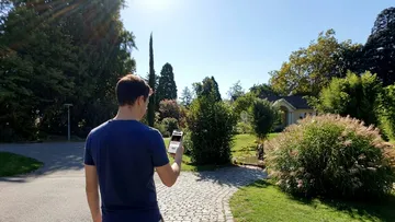 Person using smartphone in sunny garden.