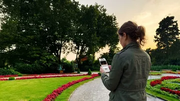 Frau benutzt Handy im Garten bei Sonnenuntergang.