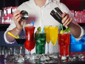 Barkeeper mixt farbige Cocktails vor einer Bar.