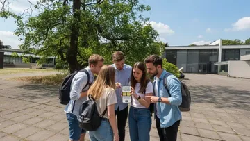 Gruppe nutzt Handy auf sonnigem Campus.