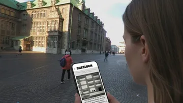 Frau liest Handy auf Kopfsteinpflasterplatz.