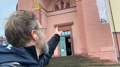 Mann zeigt auf historischen roten Gebäudeeingang.