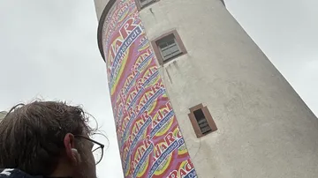 Person schaut zu hohem Turm, bewölkter Himmel.