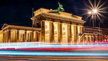Brandenburg Gate illuminated at night, with light trails.