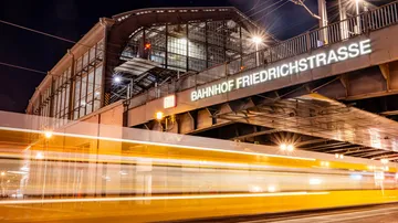Zug rast unter beleuchtetem Bahnhofsschild.