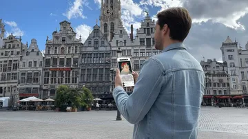 Man holds smartphone in European city square.