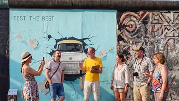 People laughing by mural with car breaking wall.