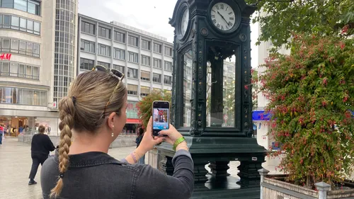 Frau fotografiert Uhrturm in städtischem Umfeld.