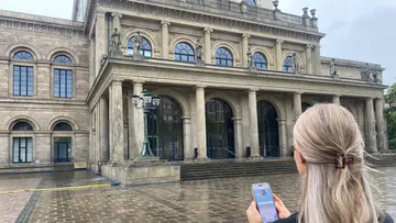 Person hält Handy vor historischem Gebäude.