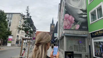 Frau fotografiert Wandbild in urbaner Straße.