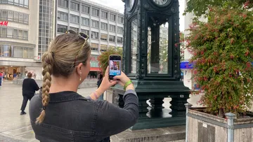 Person fotografiert einen Uhrturm auf Stadtplatz.