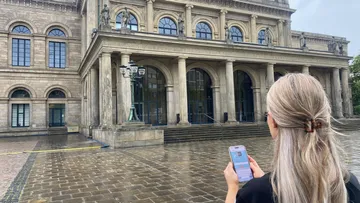Person hält Handy vor historischem Gebäude.