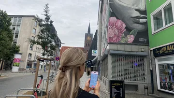 Person benutzt Handy nahe Wandgemälde in Stadtstraße.