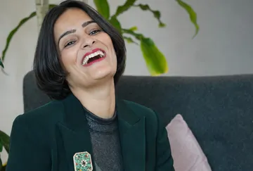 Frau lächelt, sitzt auf Couch, Pflanze dahinter.