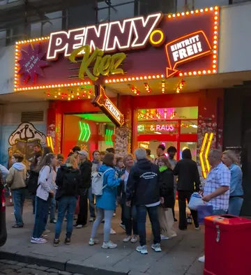 Menschenmenge vor beleuchtetem Ladeneingang nachts.