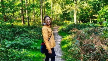 Person lächelt, geht auf Waldbodenweg.