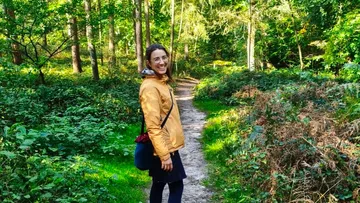 Person lächelt auf Waldweg, trägt Jacke.