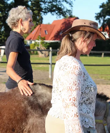 Frauen interagieren mit Esel im sonnigen Hof.