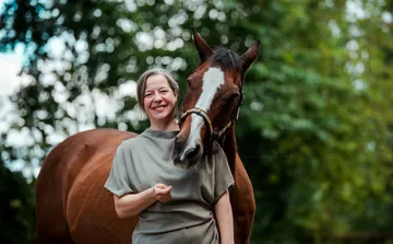 Person lächelt mit einem Pferd im Freien.