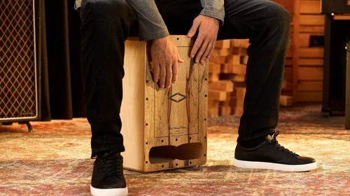 Person plays cajón on colorful carpet.