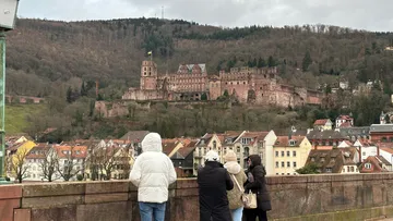 Tourists admire castle from bridge, hillside town.
