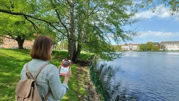 Person using smartphone by a riverside park.